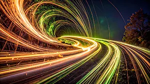 夜の道路に沿って流線型に伸びる、オレンジと黄緑の光の筋のイラスト。