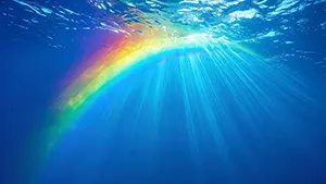深い青色の水中で水面から差し込む光の筋が美しい虹色になっている幻想的な風景