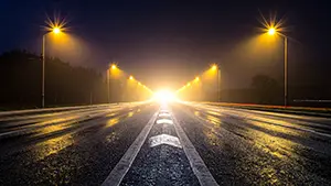 夜の高速道路で街灯と車のライトが地平線の光に向かって伸びているスピード感のある風景